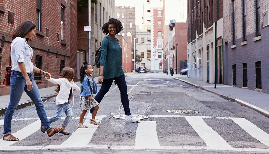 A photo of 2 adults crossing the street in a crosswalk with their children.